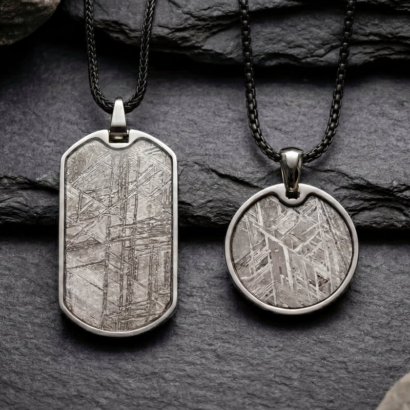 Two silver pendants on dark stone surface